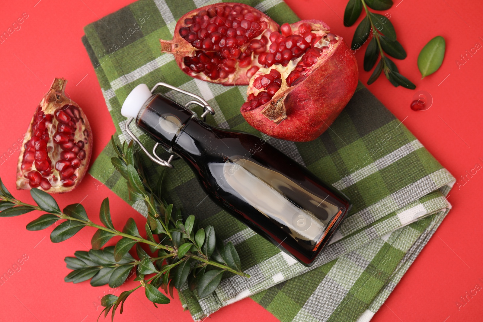 Photo of Tasty pomegranate sauce in bottle, branches and fruits on red table, flat lay