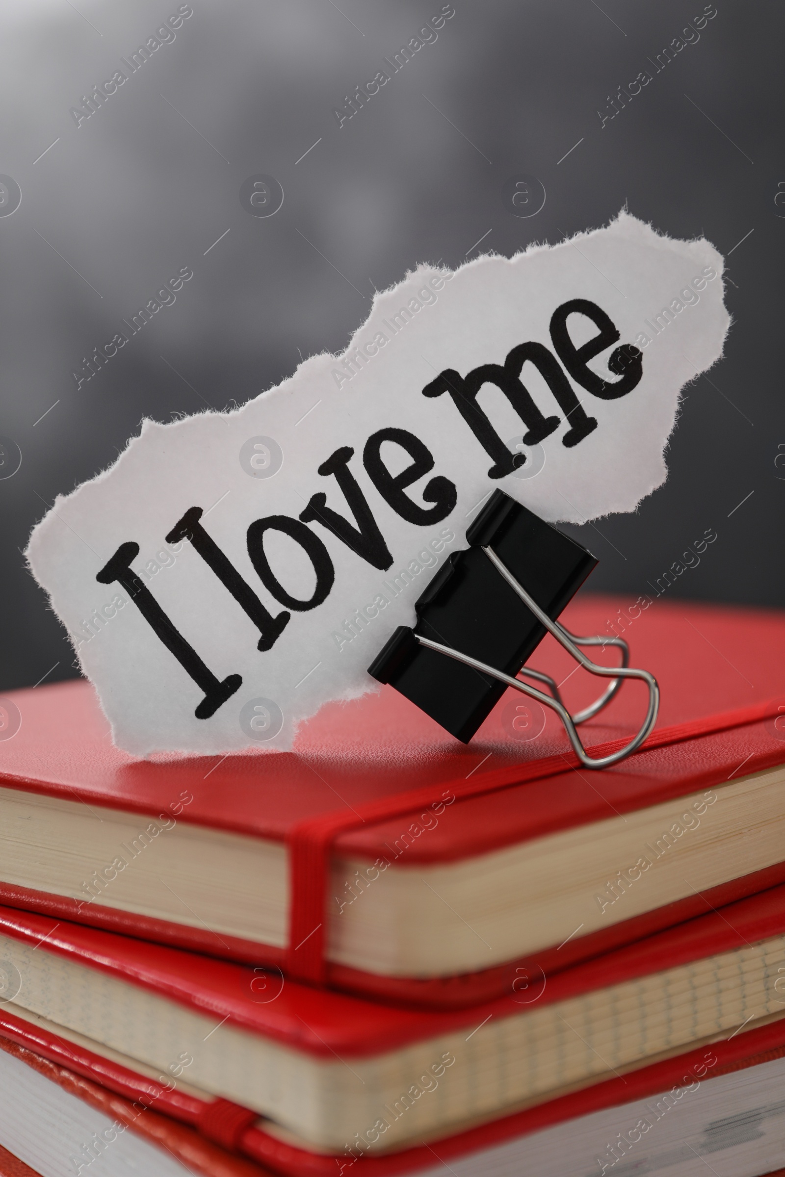 Photo of Piece of paper with handwritten phrase I Love Me and clip on notebook stack, closeup