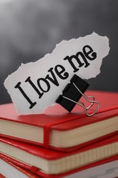 Piece of paper with handwritten phrase I Love Me and clip on notebook stack, closeup