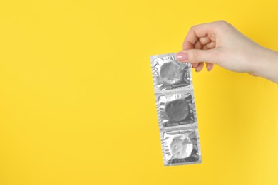 Photo of Woman holding condoms on yellow background, closeup. Space for text