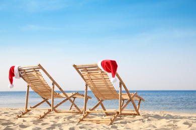 Sun loungers with Santa's hats on beach, space for text. Christmas vacation