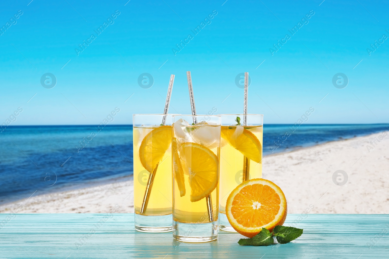 Image of Tasty refreshing drink on wooden table against sandy beach