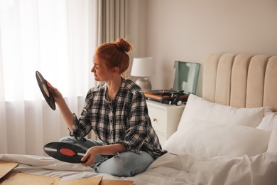 Young woman choosing vinyl disc to play music with turntable in bedroom