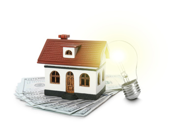 Glowing light bulb, model of house and banknotes on white background. Energy efficiency, loan, property or business idea concepts