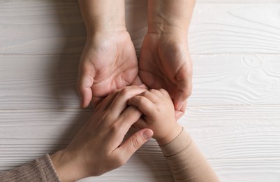 Family holding hands together at white wooden table, top view. Space for text