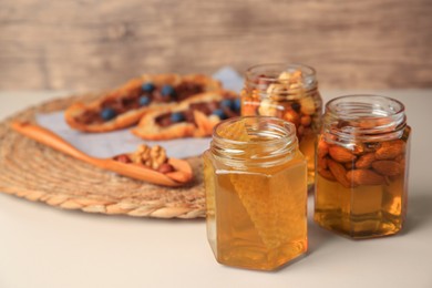 Jars with nuts and honey on beige table, space for text