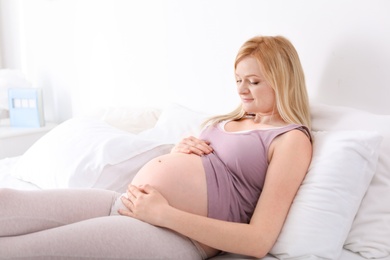 Photo of Beautiful pregnant woman resting on bed in light room