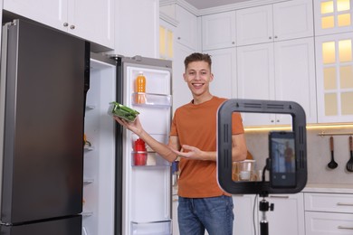 Photo of Smiling food blogger explaining something while recording video in kitchen