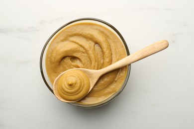 Bowl and spoon with tasty mustard sauce on white table, top view