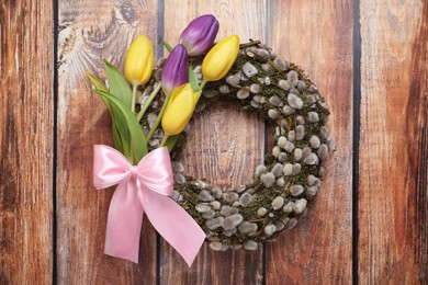 Photo of Wreath made of beautiful willow, colorful tulip flowers and pink bow on wooden background, top view