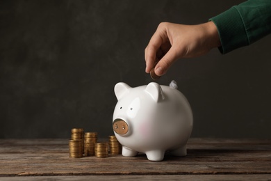 Woman putting coin into piggy bank on table against dark background