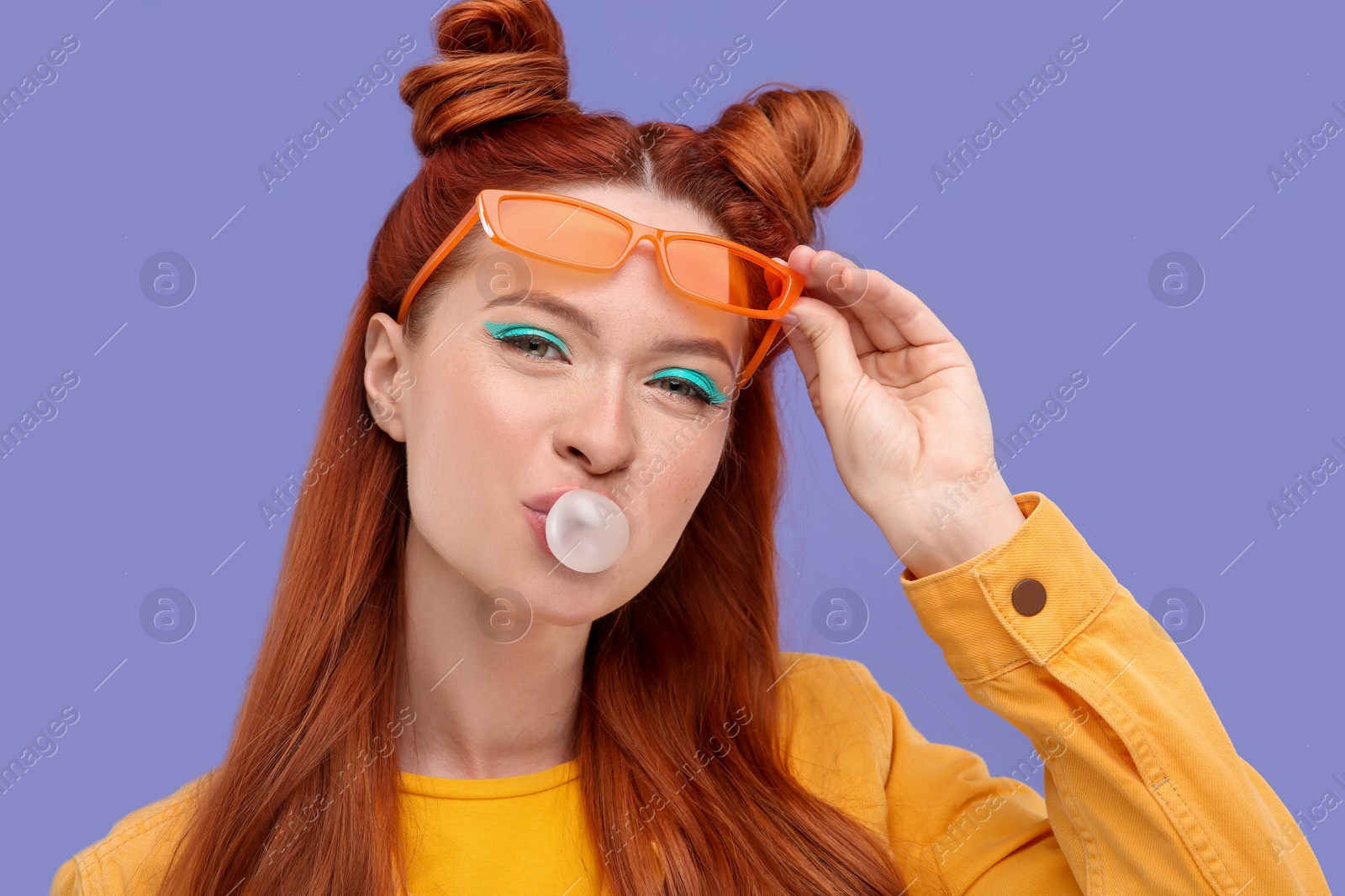 Photo of Portrait of beautiful woman with bright makeup blowing bubble gum on violet background