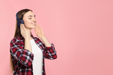 Happy woman in headphones enjoying music on pink background, space for text