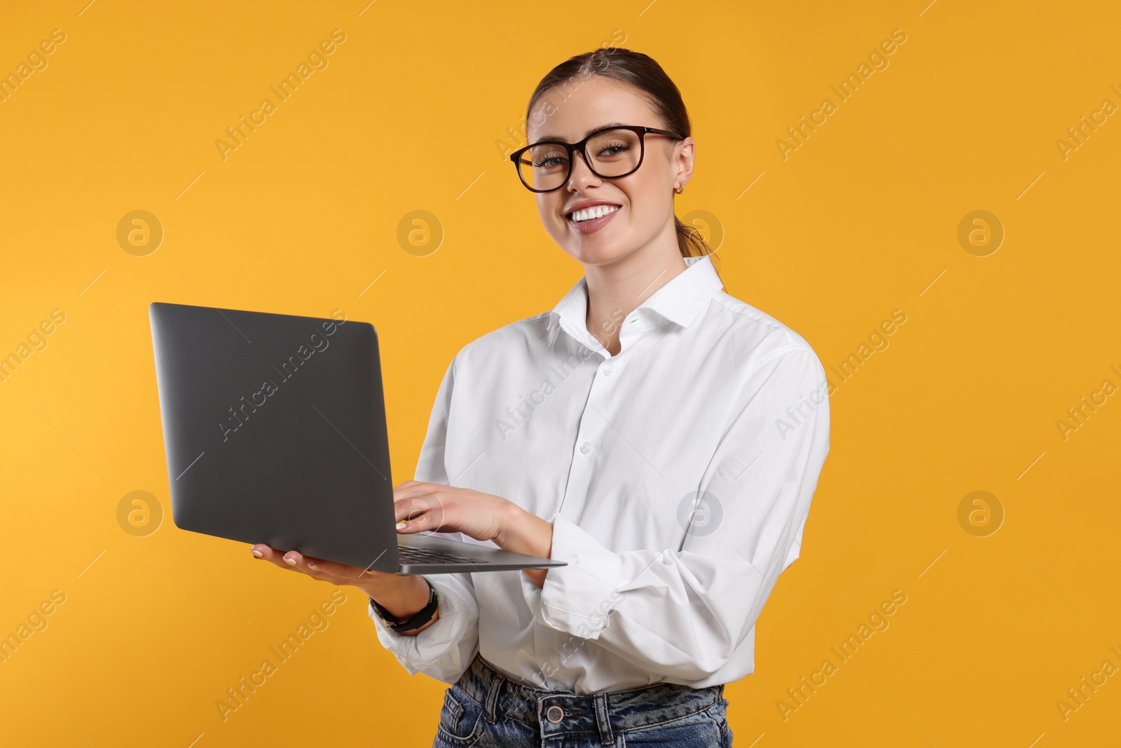 Photo of Happy woman in glasses with laptop on orange background