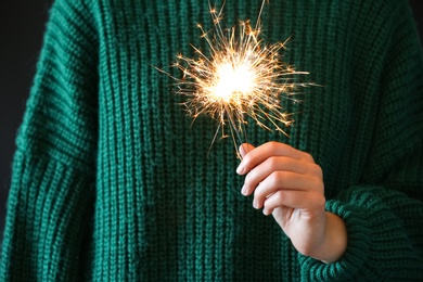 Photo of Woman in green sweater holding burning sparklers, closeup