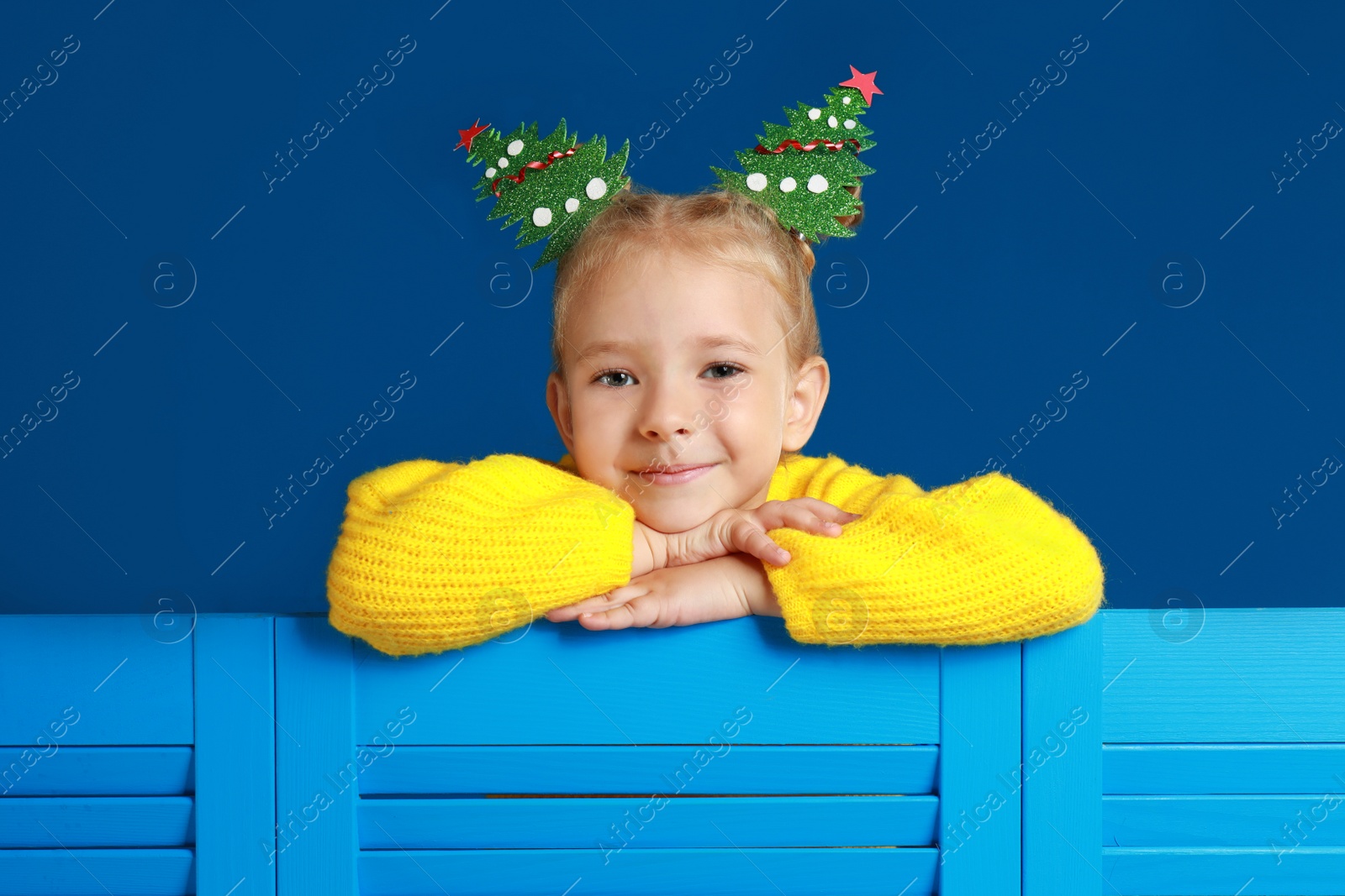 Image of Cute little girl with decorative Christmas trees on blue background