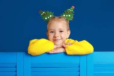 Image of Cute little girl with decorative Christmas trees on blue background