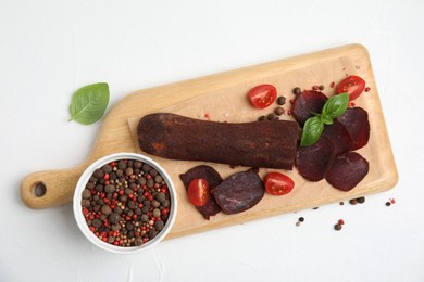 Photo of Delicious dry-cured beef basturma with basil, peppercorns and tomatoes on white table, flat lay