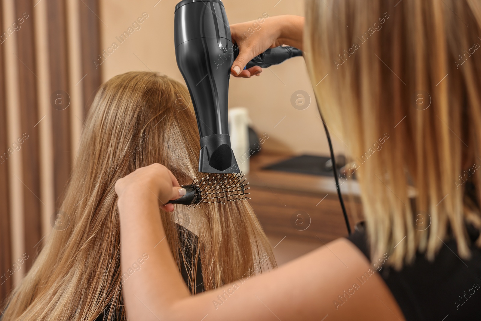 Photo of Professional hairdresser drying girl's hair in beauty salon, closeup