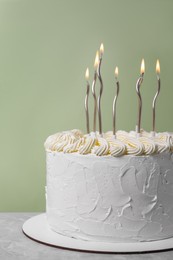 Delicious cake with cream and burning candles on grey table, closeup
