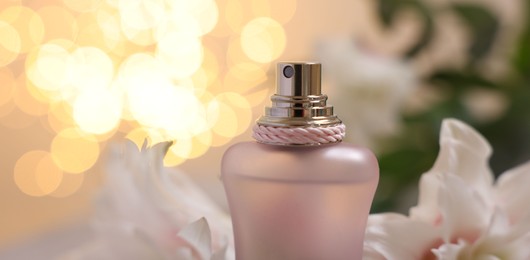 Photo of Bottle of perfume and beautiful lily flowers against beige background with blurred lights, closeup. Space for text