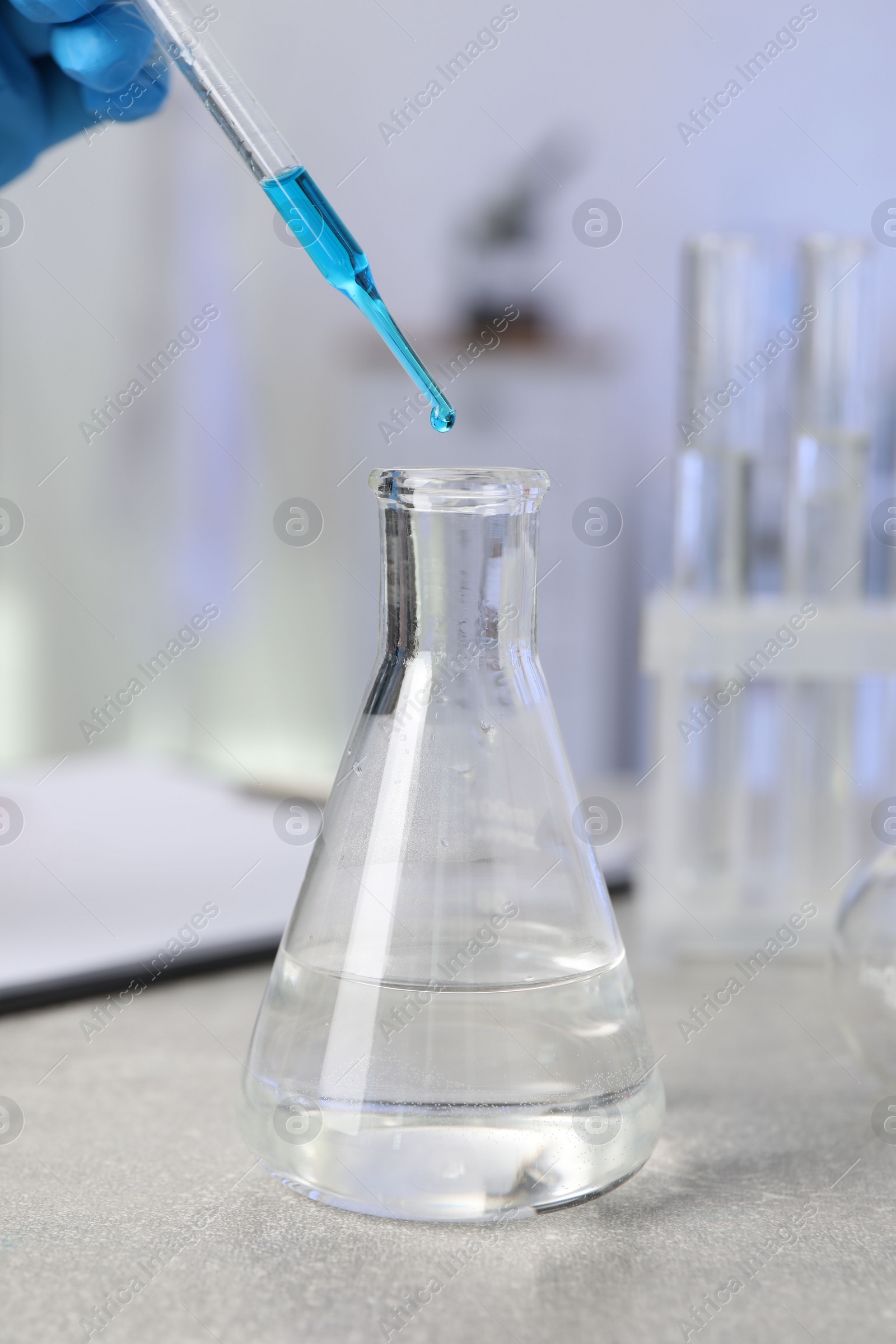 Photo of Laboratory analysis. Woman dripping liquid into flask at light grey table, closeup