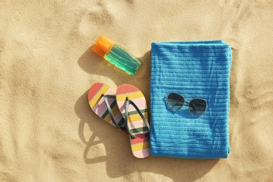 Flat lay composition of beach objects and towel on sand, space for text