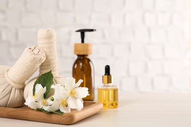 Beautiful jasmine flowers, herbal bags and skin care products on white wooden table, space for text