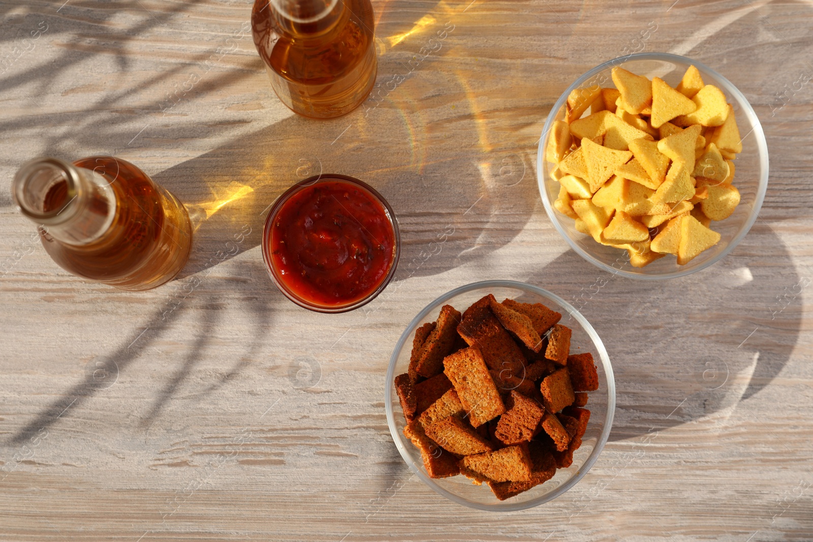Photo of Different crispy rusks, beer and dip sauce on wooden table, flat lay