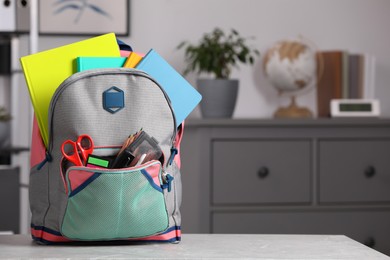 Photo of Children's backpack with different school stationery on table indoors, space for text