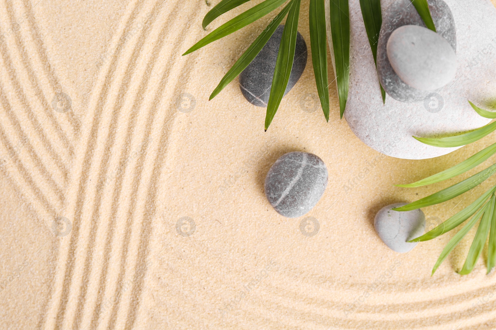 Photo of Zen garden stones and green leaves on sand with pattern, flat lay. Space for text