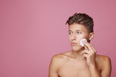 Photo of Handsome man cleaning face with cotton pad on pink background, space for text