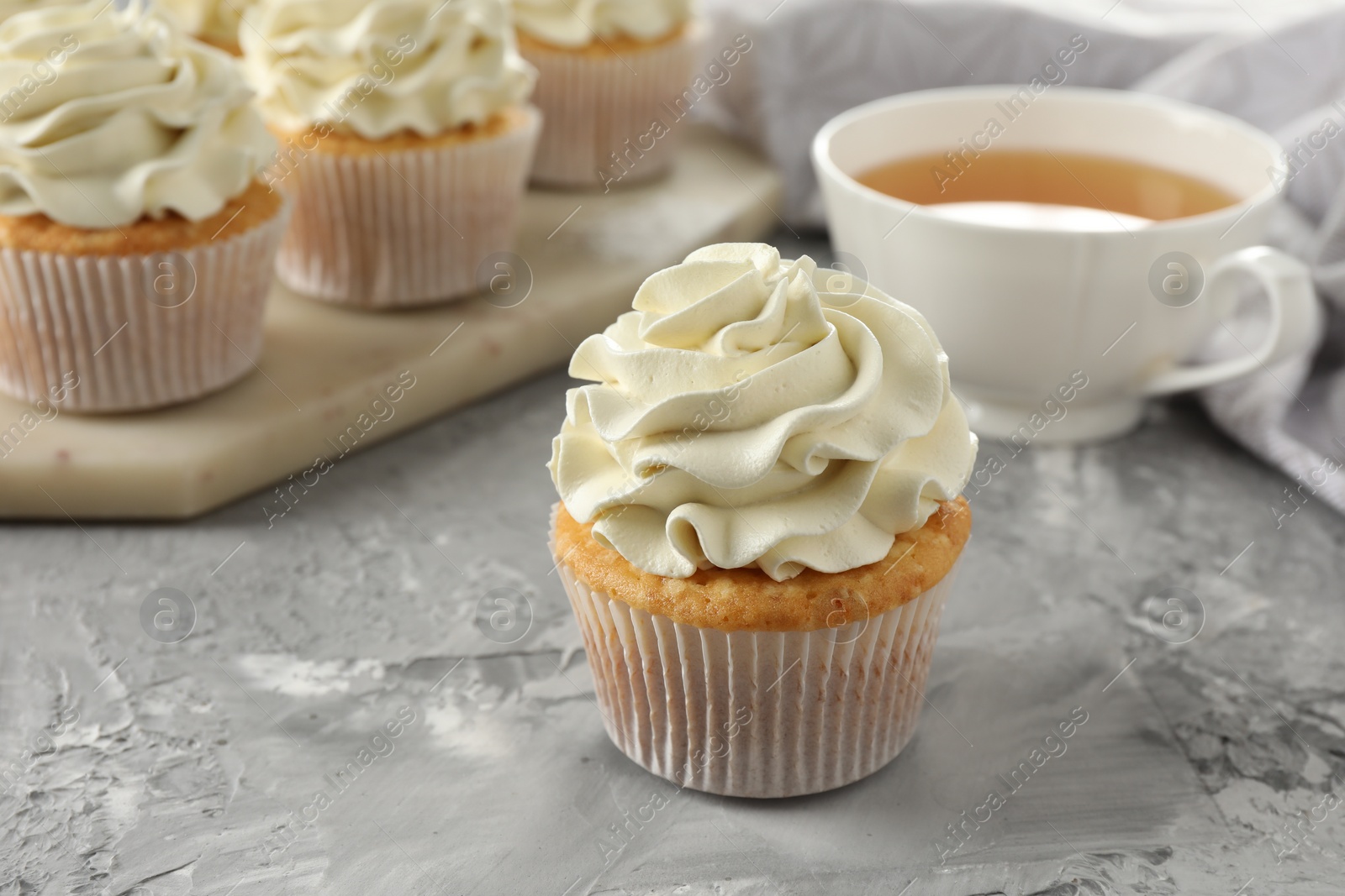 Photo of Tasty cupcakes with vanilla cream on grey table, closeup