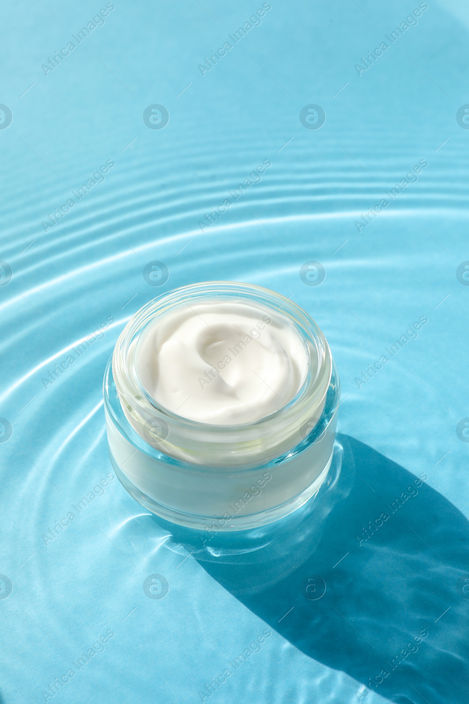 Photo of Jar with moisturizing cream in water on light blue background