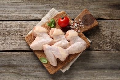 Photo of Raw chicken wings with basil, tomato and spices on wooden table, top view