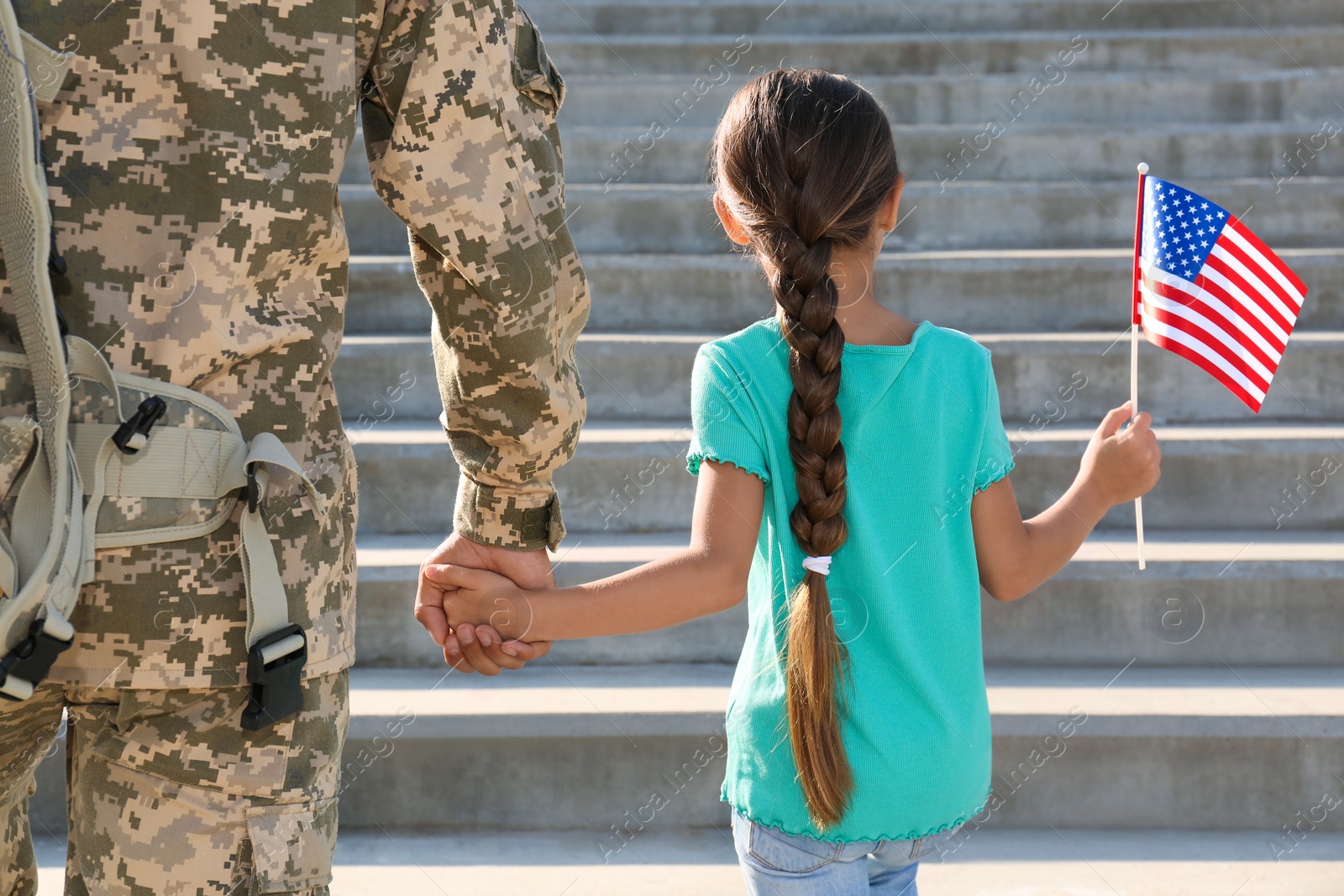 Photo of Soldier and his little daughter with American flag outdoors, back view. Veterans Day in USA