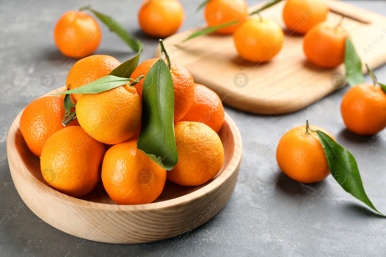 Photo of Fresh tangerines with green leaves on grey table, closeup