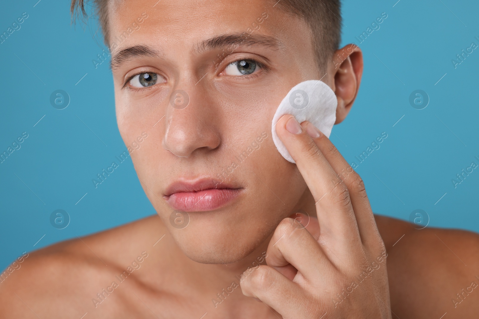 Photo of Handsome man cleaning face with cotton pad on light blue background