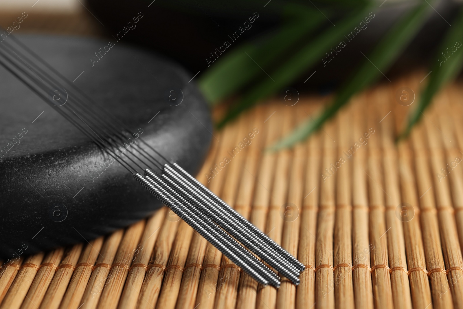 Photo of Acupuncture needles and spa stone on bamboo mat, closeup