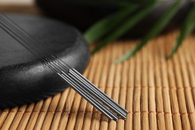 Photo of Acupuncture needles and spa stone on bamboo mat, closeup