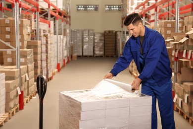 Photo of Worker wrapping boxes in stretch film at warehouse