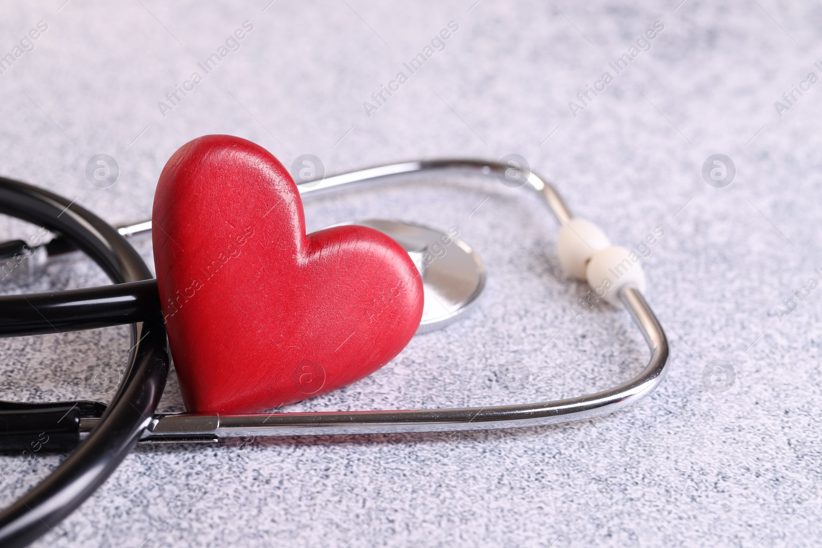 Photo of Stethoscope and red heart on grey stone table. Space for text