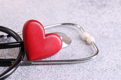 Photo of Stethoscope and red heart on grey stone table. Space for text