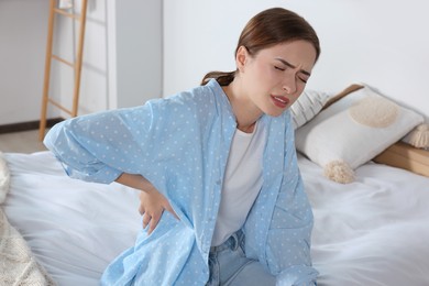 Photo of Woman suffering from back pain while sitting on bed at home. Symptom of scoliosis