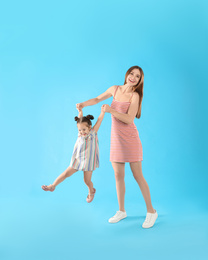 Young mother and little daughter having fun on light blue background