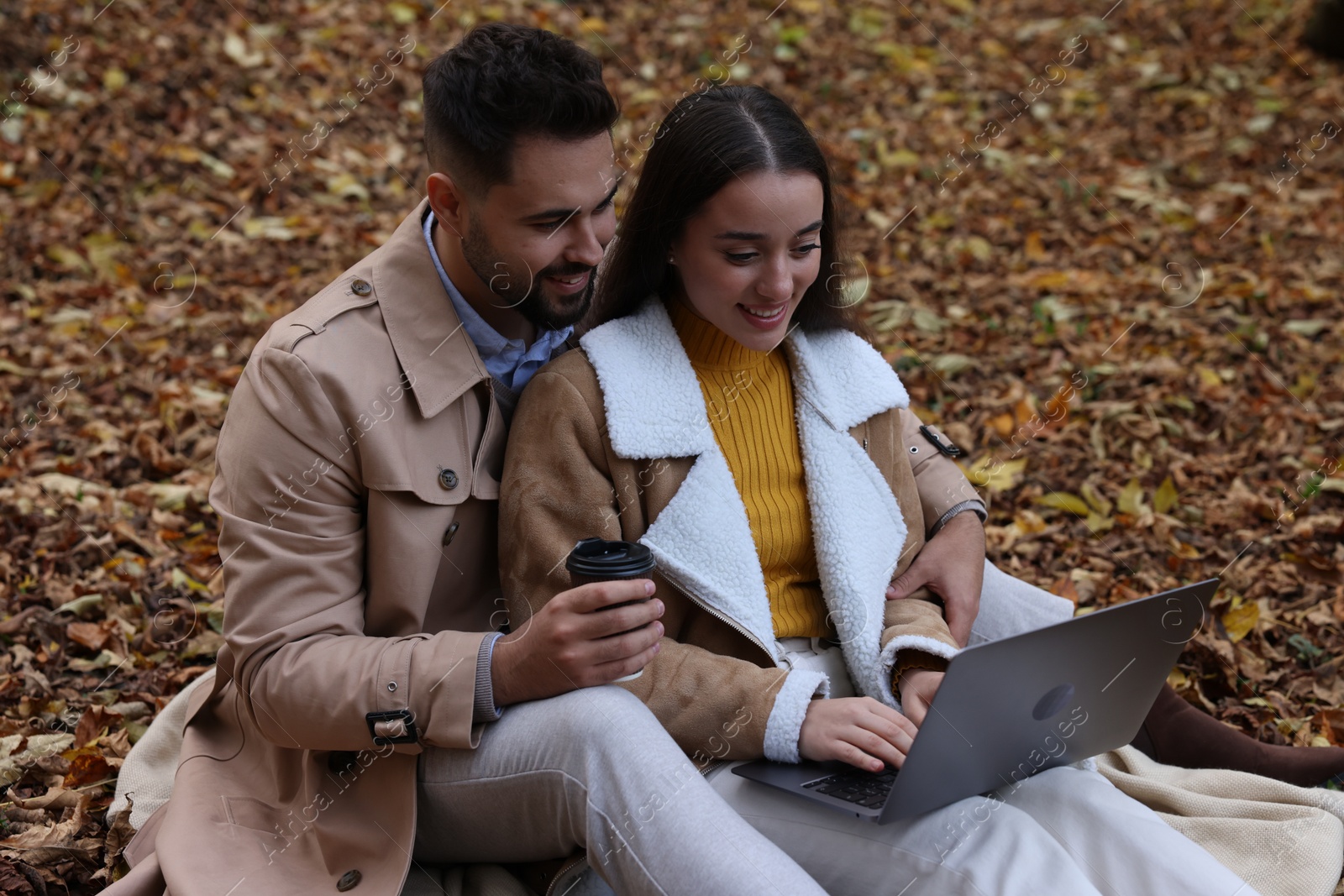 Photo of Happy young couple with laptop spending time together in autumn park