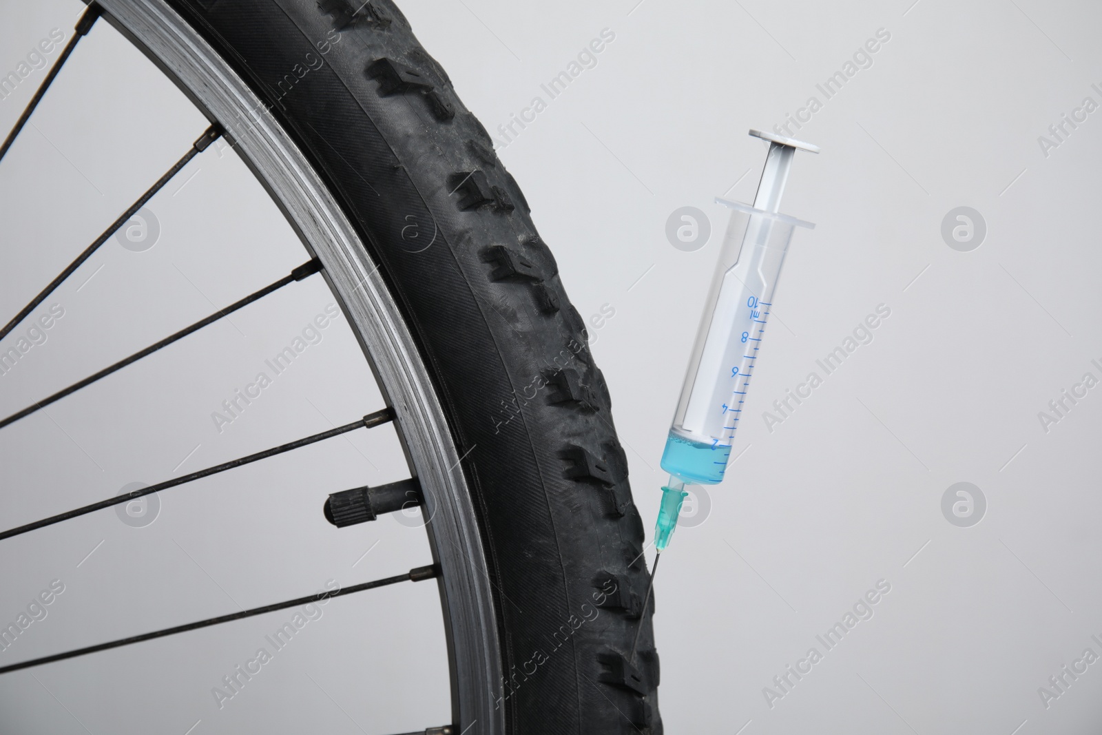 Photo of Bike wheel with syringe on light background, closeup. Using doping in cycling sport concept