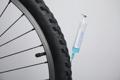 Photo of Bike wheel with syringe on light background, closeup. Using doping in cycling sport concept