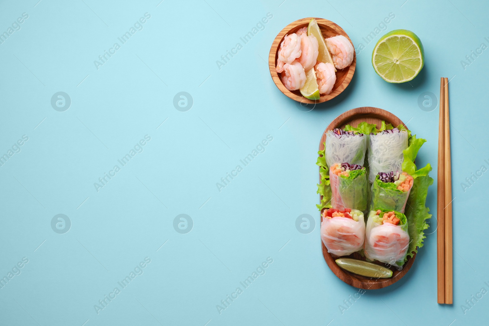 Photo of Delicious spring rolls, shrimps, lime and chopsticks on light blue background, flat lay. Space for text