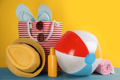 Photo of Colorful inflatable ball and different beach accessories on light blue wooden table against yellow background